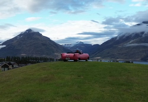 The little pink car parked above the lake with mountains beyond