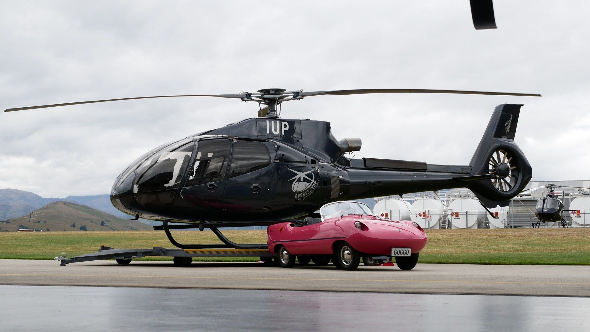 The little pink car beside an Over The Top helicopter
